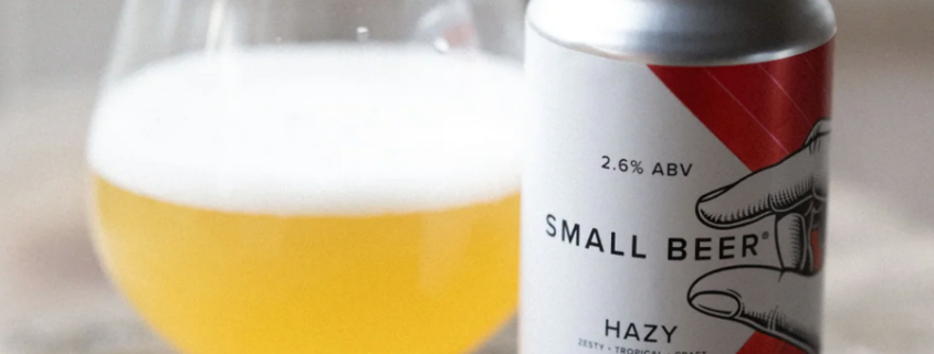 Can of Small Beer hazy craft beer beside a glass on a wooden table.